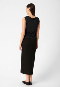 Černý bezrukávový top s draped výstřihem, doplněný dlouhou černou sukní. Hladká tkanina, přiléhavý design a jemné nařasení vzadu.