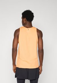 Orange ærmeløs tanktop lavet af letvægtsstof. Har en rund hals og et lille sort logo-accent på bagsiden.