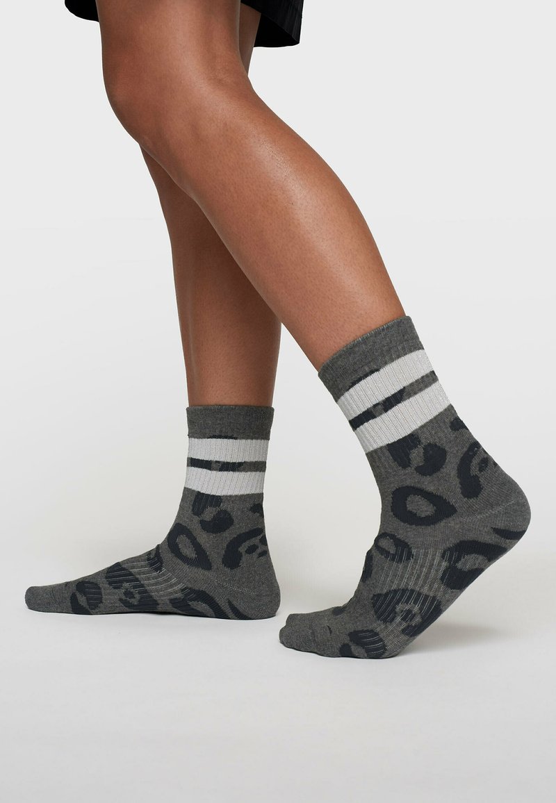 Calcetines grises con un patrón de leopardo en gris oscuro, con un puño acanalado y dos franjas blancas en la parte superior.