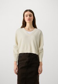 Gaiši krēms V veida kakla svīteris ar garām piedurknēm, kombinēts ar tumšu denima zīda svārku. Minimālistisks dizains, mīksta tekstūra un brīvā piegriezumā.