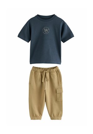 Dunkelblaues Baumwoll-T-Shirt mit rundem Logo; kombiniert mit beigefarbenen Jogginghosen mit elastischem Bund und seitlicher Cargo-Tasche.