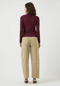 Burgundowy, prążkowany top z długim rękawem, dopasowany fason, zestawiony z beżowymi spodniami o szerokich nogawkach i czarnymi sandałami na obcasie. Widok tylni stroju.