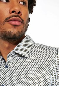 Geprinte shirt met een witte basis en kleine zwarte en gouden cirkelvormige ontwerpen, een klassieke kraag en blauwe knopen.