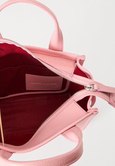 Sac à main en cuir rose ouvert avec fermeture éclair argentée, montrant l'intérieur en tissu rouge foncé et une étiquette Marc Jacobs à l'intérieur.