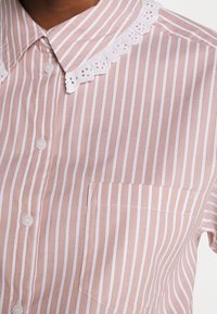 Stribet skjorte i blødt stof, med pink og hvide lodrette striber, en hvid blonderkantet krave og en brystlomme.