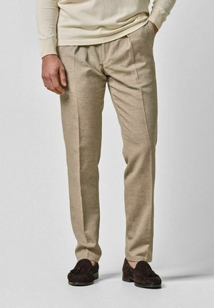 Pantalones de lino beige con corte recto, con detalle de pliegues en la parte delantera. Combinados con mocasines de ante oscuro. Sencillo y elegante.