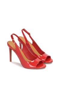 Punaiset patenttipintaiset slingback-korkokengät avoimella varpaalla, stiletto-korko ja koristeellinen nilkkaremmi, jossa on kultasolka.