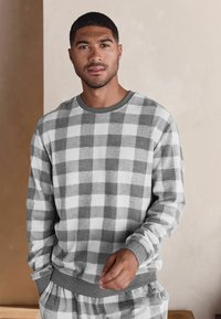 Grau-weißer Karodesign-Pullover mit langen Ärmeln, Rundhalsausschnitt und gerippten Bündchen; kombiniert mit passenden Hosen. Weicher Stoff.