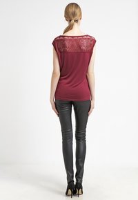 Top corto burdeos de manga corta con detalles de encaje en los hombros, combinado con pantalones de cuero ajustados negros y tacones. Textura de tela suave.