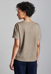 Top a maniche corte color khaki con vestibilità morbida, finitura testurizzata e orli arrotolati. Il retro presenta un'emulsione curva sottile.