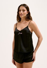 Zwarte satijnen camisole met dunne spaghettibandjes, voorzien van geborduurde tekst in het roze en bijpassende satijnen shorts. Soepele textuur, relaxte pasvorm.