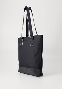 Black tote bag made of durable fabric, featuring a solid body, white-striped handles, and a contrasting black bottom panel.