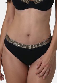 Fekete bikini alsó, amelyet egy széles arany és ezüst fémes díszítésű öv jellemez, sima anyagból készült, alacsony derékú kivitelben.