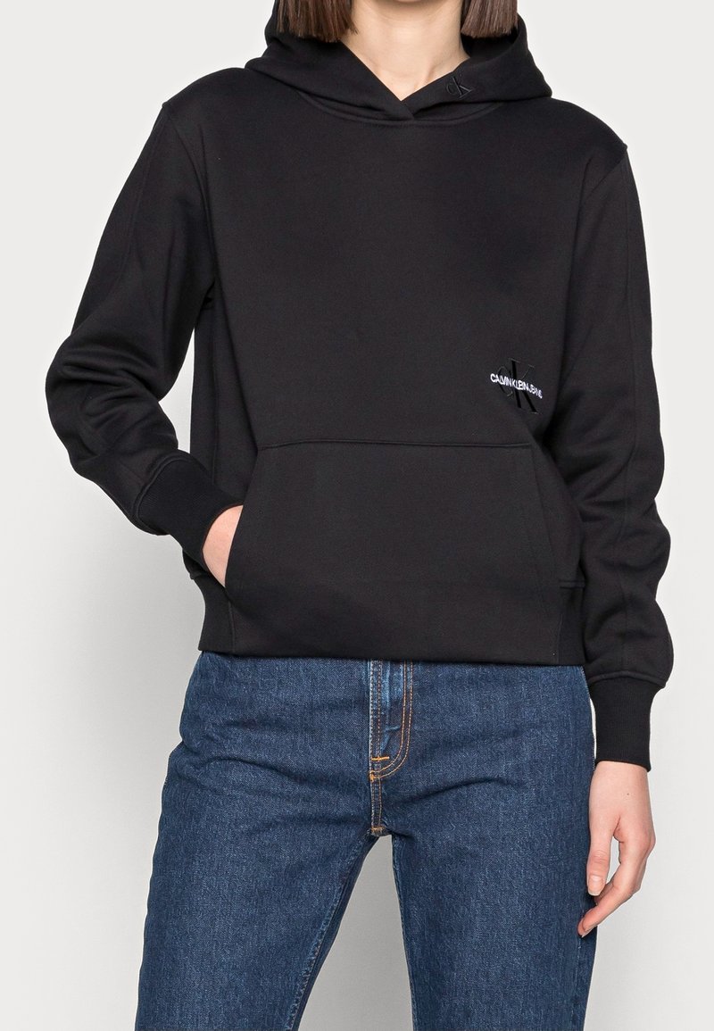 Sudadera con capucha negra, hecha de un tejido suave. Cuenta con un bolsillo frontal, puños acanalados y un pequeño logo en el pecho como detalle.