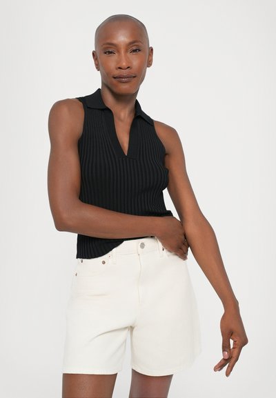 Black ribbed sleeveless top with a V-neckline, paired with white denim shorts featuring front pockets and copper-tone hardware accents.