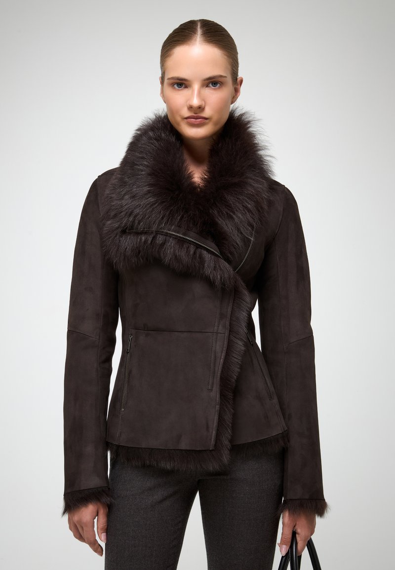 Chaqueta de ante marrón oscuro con cuello de piel sintética, parte frontal asimétrica, bolsillos con cremallera y detalles texturizados en las mangas y el dobladillo.