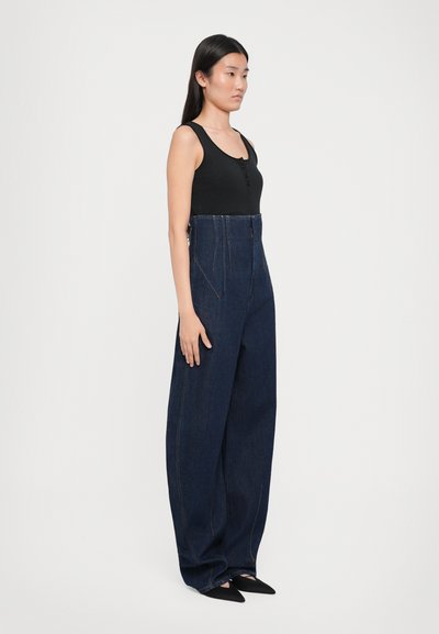 Pantaloni din denim albastru cu talie înaltă, cu picioare largi, având cusături în contrast și buzunare frontale, asortați cu un top negru mulat.