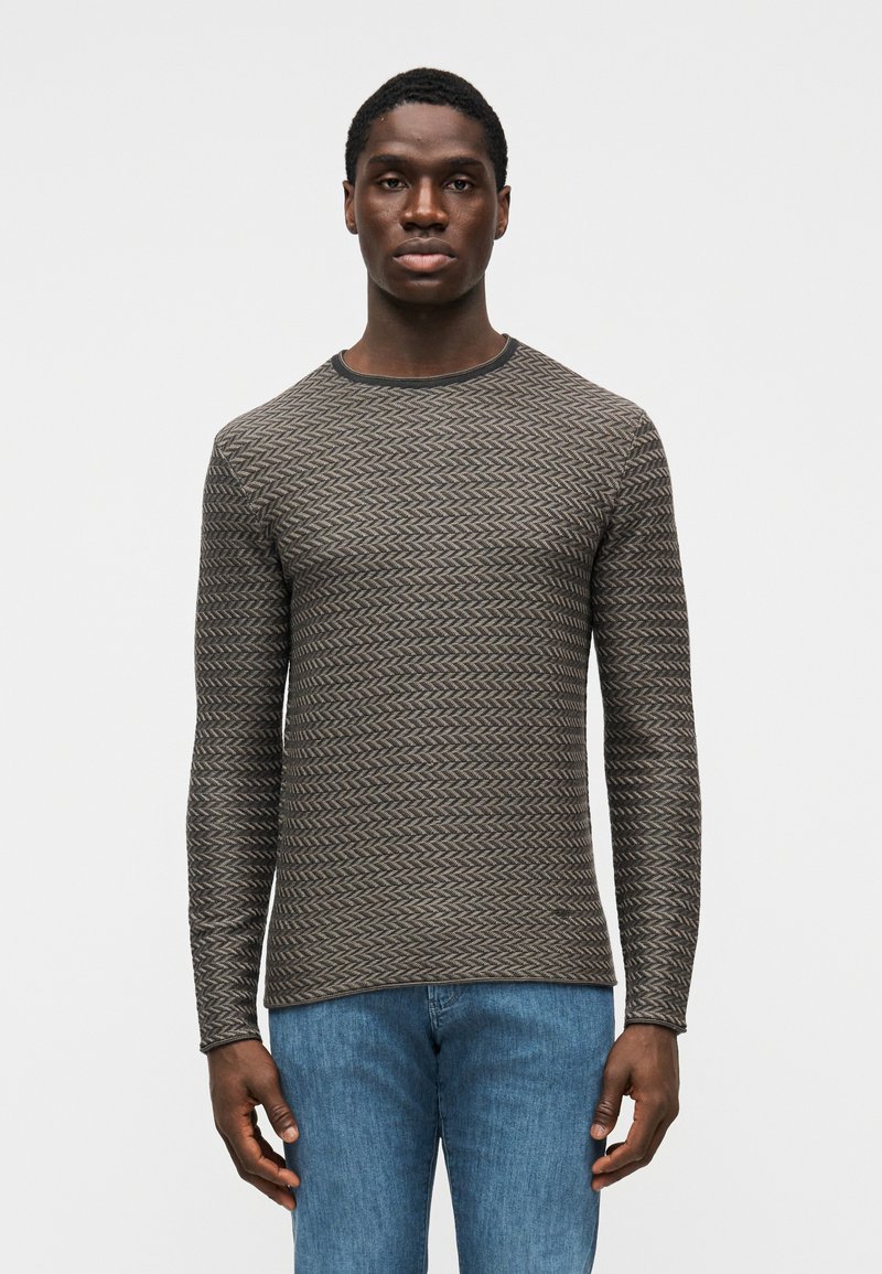 Camisa de manga comprida com padrão em cinzento escuro com design de espinha de peixe, decote canelado e tecido texturizado. Usada com jeans azuis.