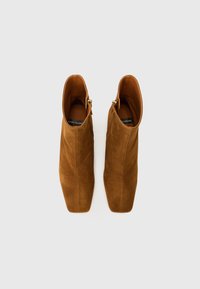 Botas de tobillo de ante marrón con una textura suave, puntera afilada y cremalleras doradas en los laterales. La parte superior es elegante y ceñida.