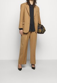 Oversized béžový blazer s odpovídajícími širokými kalhotami, námořnická blůza pod ním a černé lodičky s špičkou. Černá a károvaná kabelka.