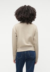 Sweatshirt bej, cu guler rotund, cu o croială lejeră și tiv ribbed. Material moale din bumbac, cu cusături la umeri tip drop și cusături minime.