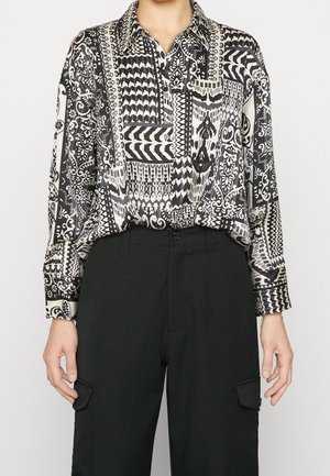 Mustavalkoinen kuvioitu pitkähihainen paita, joka on puettu korkeavyötäröisten mustien cargo-housujen sisään, joissa on läppätaskut.