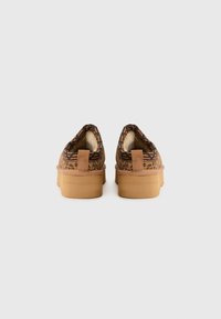 Bruine slip-on schoenen met een patroon, een gestructureerde buitenkant, een zachte voering en een dikke rubberen zool, met een lus aan de hiel voor gemakkelijk aan- en uittrekken.