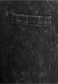 Svart denimtyg har en texturerad yta med en blekt, slitet utseende. En rektangulär ficka syns på högra sidan.