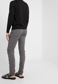 Pantalon gris slim en tissu doux, taille mi-haute, associé à des sandales noires à rayures multicolores, vu de dos.