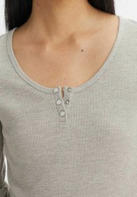 Haut gris côtelé à manches longues avec un col rond et trois boutons-pression argentés à l'avant. Texture douce avec une coupe ajustée.