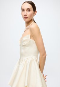 Strapless ivory satin dress with a fitted bodice, flowing skirt, and soft drape. Paired with a pearl necklace for detail.