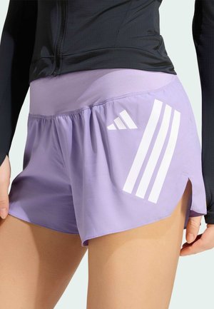 Close-up af en person iført lilla Adidas træningsshorts med hvidt logo og striber, kombineret med en sort langærmet top.
