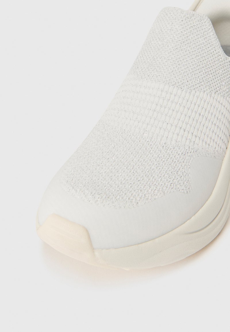 Jasnoszare buty typu slip-on z teksturowanym dzianinowym wierzchem i gładką, lekko wyprofilowaną podeszwą. Okrągły nosek z subtelnymi akcentami wzorniczymi.