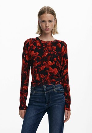 Suéter de manga larga con estampado floral rojo y cuello de canalé, combinado con jeans de mezclilla azul oscuro. El suéter tiene un ajuste ceñido y una textura suave.