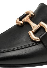 Black leather shoe featuring a metallic gold hardware buckle, with a smooth texture and pointed toe design. Detailed stitching along the edge.