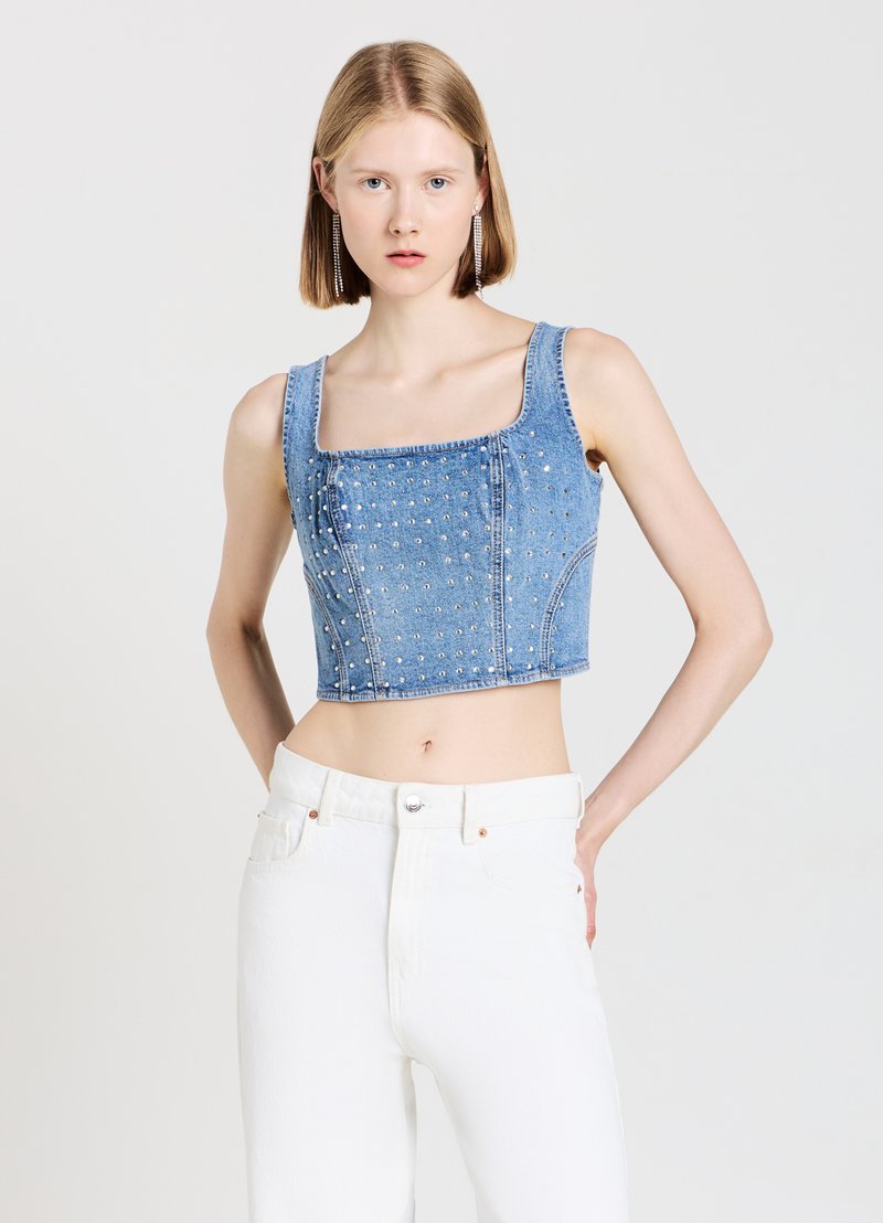 Top in denim tagliato con scollatura quadrata, tessuto blu chiaro, adornato con borchie argentate, abbinato a pantaloni bianchi a vita alta.