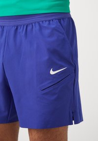 Karaliskā zilā krāsā sporta šorti, izgatavoti no viegla auduma. Aprīkoti ar slēptu rāvējslēdzēju kabatu un baltu Nike logo sānos.