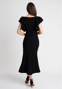 Czarna midi sukienka z falbaniastymi krótkimi rękawami, dopasowanym gorsetem, rozkloszowanym dołem i zamkiem z tyłu, w zestawie z czarnymi szpilkami.