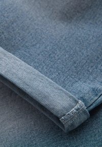Tela de denim en un color azul desvaído, con un dobladillo enrollado y costuras visibles, además de una textura suave. La superficie muestra un sutil patrón de tejido.