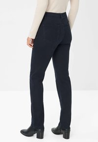 Jean noir foncé slim, doté de deux poches arrière. Porté avec un haut ajusté à rayures de couleur claire et des bottes à talons noires.