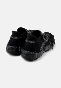 Black knit athletic shoes with speckled black soles, black and white laces, and sock-like ankle collars shown from rear side.