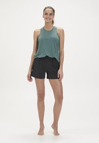 Tanktop van groen gestreepte stof gecombineerd met zwarte sport shorts. De outfit heeft een relaxte pasvorm en lichtgewicht materiaal.