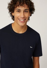 Navyblauwe katoenen T-shirt met een ronde hals en korte mouwen, voorzien van een klein wit hondenlogo op de linkerbortszijde. Zachte textuur.