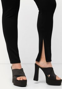 Zwarte leggings met een slim fit en zijritsen aan de zoom, gecombineerd met chunky zwarte sandalen met hoge hakken en een kruisbandontwerp.