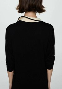 Pullover nero con maniche a tre quarti, caratterizzato da un colletto crema e bordi neri. Il tessuto appare morbido e lavorato a maglia.