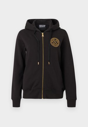 Svart hettejakke med glidelås, hette, svarte snorer, gullfarget glidelås og rund gullfarget Versace Jeans Couture-logo på venstre bryst.