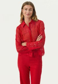 Červená čipkovaná košeľa s button-up zapínaním a textúrovaným károvaným vzorom, s dlhými rukávmi a květinovými strihovými akcentmi na manžetách a spodnom leme.