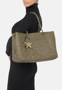 Oliivinvihreä tikattu käsilaukku, jossa on metalliset tähtikoristeet, ketjuhihna ja vetoketjullinen tasku. Sileä pinta, suorakulmainen muoto.