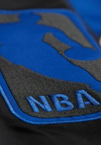 NBA-Logo mit einer abstrakten Spieler-Silhouette in Blau auf einem grau-schwarzen Hintergrund, mit erhabenem Stickerei-Effekt für zusätzliche Textur.