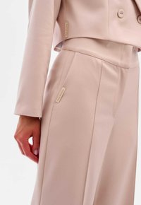Lichtroest gepersonaliseerd pak met een cropped jasje en hoge taille broek, gladde textuur, met een klein label aan de zijkant.